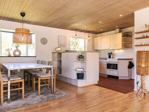 A modern kitchen with wooden cabinets, a dining area with a table and chairs, and a large window providing natural light. - 6 Person Holiday Home in Vaeggerlose (Vaeggerlose)