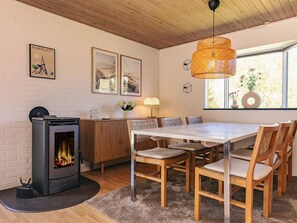 A cozy room with a wood-burning stove, a dining table with chairs, and artwork on the walls. - 6 Person Holiday Home in Vaeggerlose (Vaeggerlose)