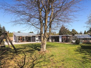 Ein Wohnhaus mit einem Garten, einer Terrasse mit Gartenmöbeln und einem Gewächshaus.