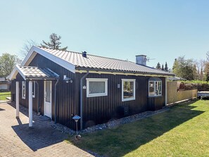 A single-story building with a sloped roof, a small porch, and a fenced yard. - 6 Person Holiday Home in Vaeggerlose (Vaeggerlose)