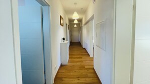 Un corridoio con pavimento in legno, pareti bianche e porte che conducono a diverse stanze.