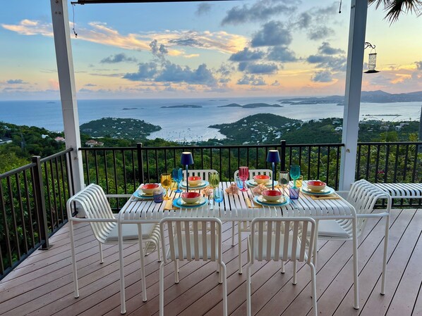 A table set for dining with a scenic ocean view, white chairs, and a railing.