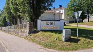 A hotel sign for 'Hotel NewBed' with a stone wall and trees in the background. - Hotel New Bed (Oskarshamn)