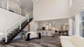 A spacious living area with a modern staircase, a kitchen with white cabinets, and a dining area with a brick wall backdrop.