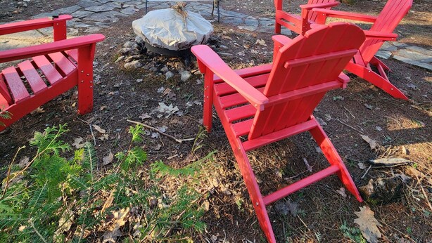 A cabin with a deck, red Adirondack chairs, and a stone fire pit. - 
Kawagama Shoreline - Private Waterfront Cottage on Kawagama Lake (Dorset)