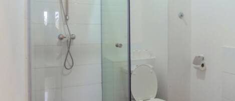Un bagno con doccia vetrata, un water e un piccolo tappeto a pavimento.