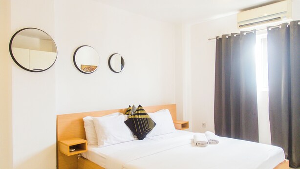 Een net opgemaakt bed met witte lakens, twee nachtkastjes en twee spiegels aan de muur.