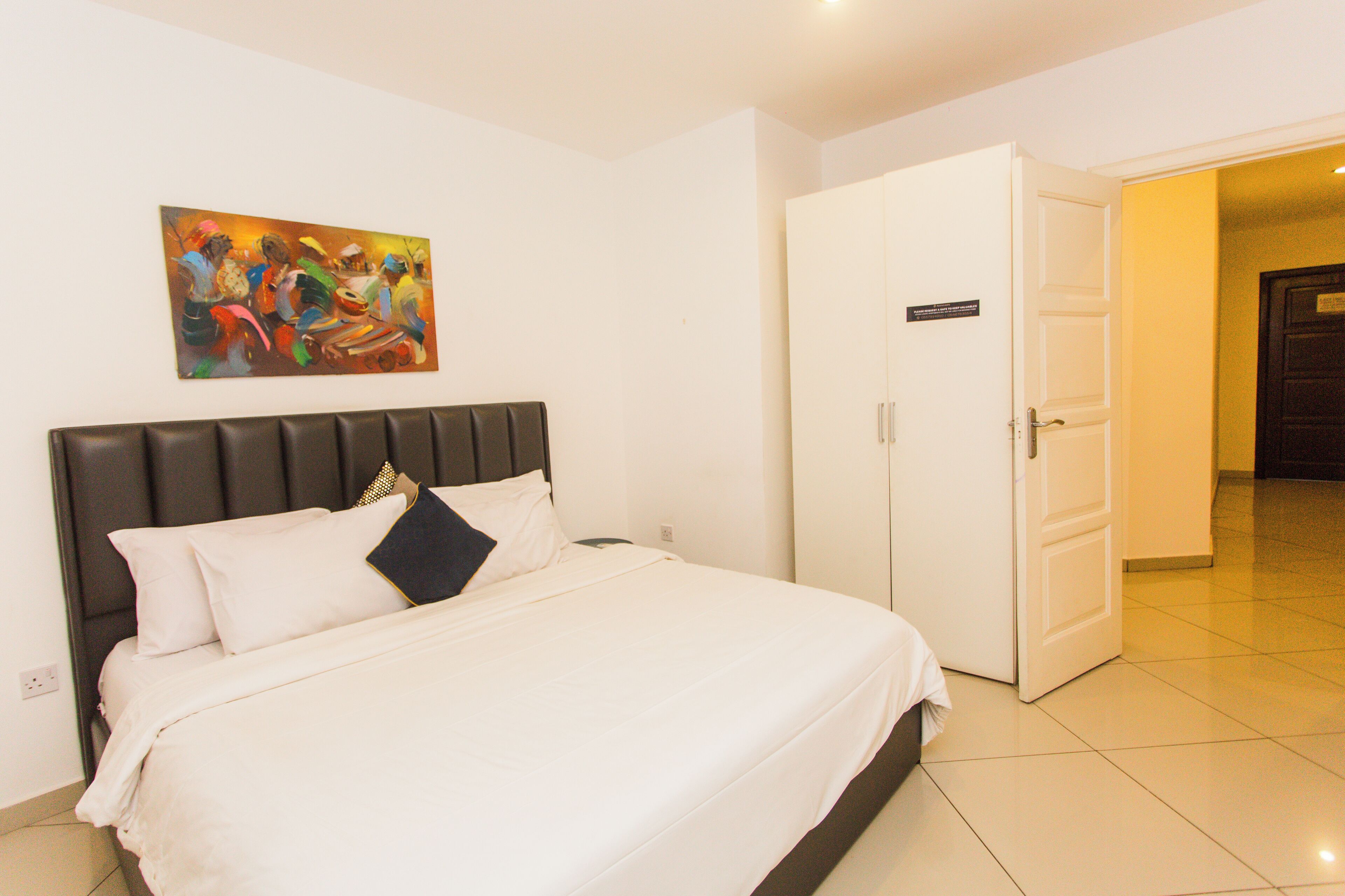 Una habitación de hotel con una cama, un cuadro en la pared, un armario y una puerta que da a otra habitación.
