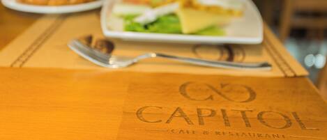 Une table en bois avec une assiette de nourriture et une fourchette. La table porte un logo sur lequel on peut lire « CAPITOL CAFE & RESTAURANT ».