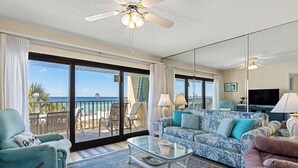 A spacious living room with a large glass door leading to a balcony, a ceiling fan, and a television.