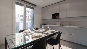 A modern kitchen with white cabinets, a glass dining table, and a view of buildings outside. - Italianway Comfort - Lazzaro Papi 14 C (Milan)