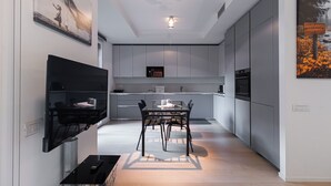 A modern kitchen with grey cabinets, a dining table with chairs, and a black TV mounted on the wall. - Italianway Comfort - Lazzaro Papi 14 C (Milan)