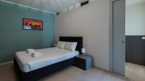 A modern hotel room with a single bed, a bedside table, a nightstand, a wall-mounted painting, and a door. - Italianway Comfort - Lazzaro Papi 14 C (Milan)
