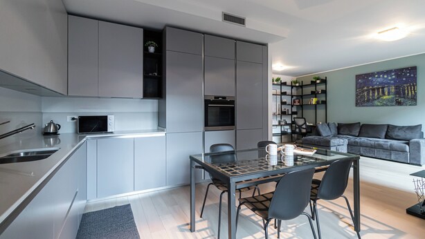 A modern kitchen with integrated appliances, a dining area with a glass table, and a living room with a sofa and bookshelf. - Italianway Comfort - Lazzaro Papi 14 C (Milan)