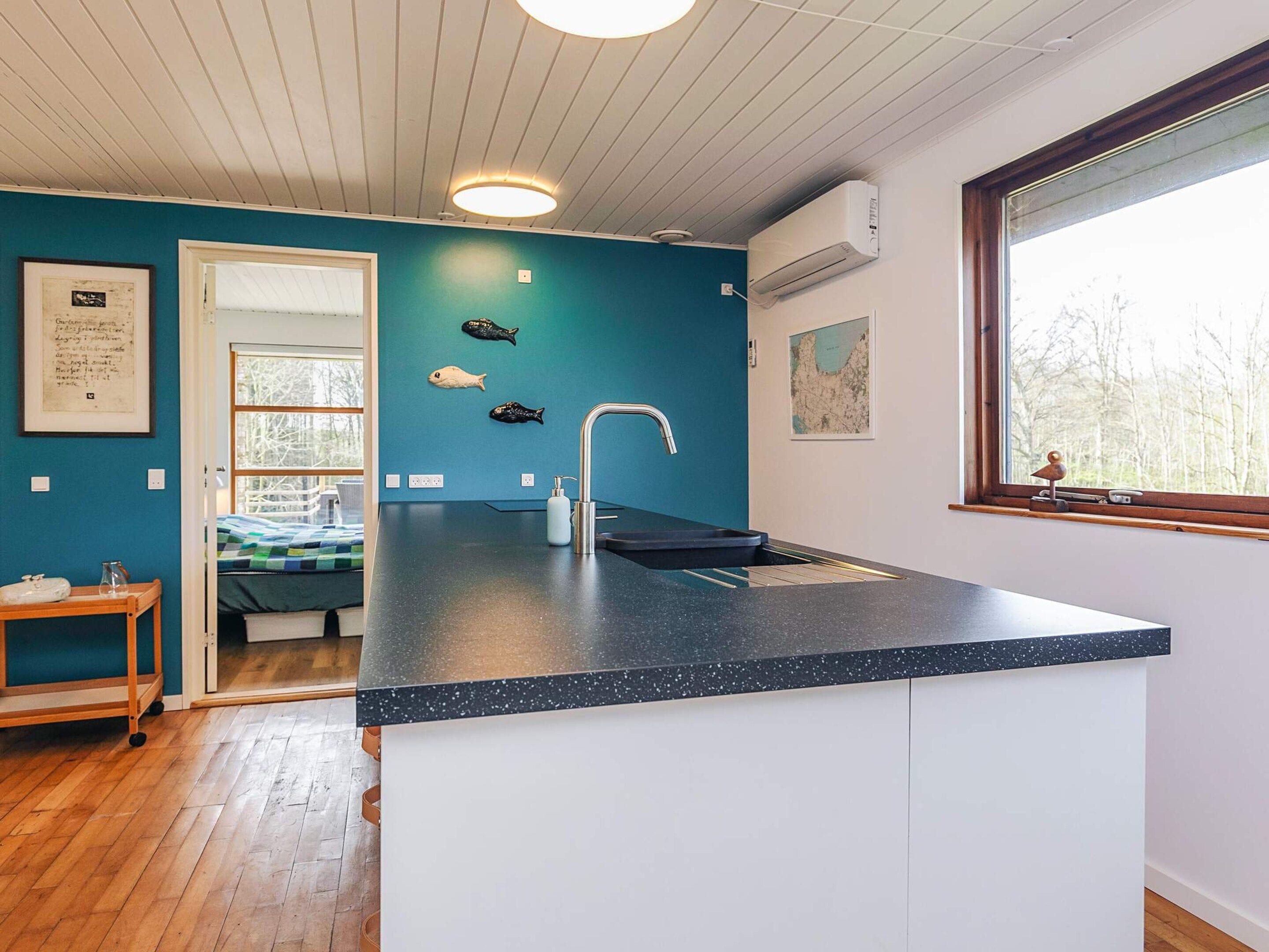 Una cocina moderna con encimera oscura, un lavabo y una ventana con vistas a árboles.