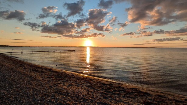A sunset over a calm body of water with a wooden pier extending into the water. - 6 Person Holiday Home in Asperup (Middelfart)