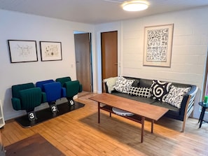 A room with a wooden floor, a sofa with patterned cushions, a coffee table, and three chairs with numbers on the floor. - 6 Person Holiday Home in Asperup (Middelfart)