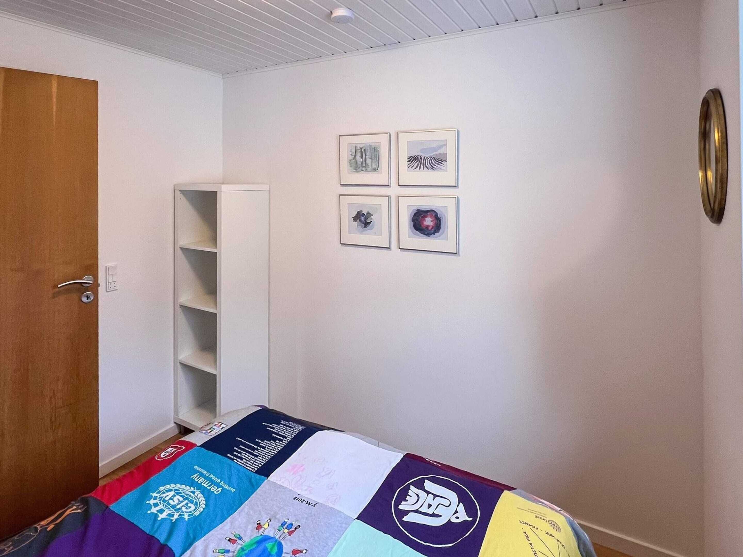 A bedroom with a bed, a wardrobe, and four framed pictures on the wall.
