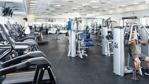 Une salle de sport équipée de tapis de course, d’appareils de musculation et où une personne utilise un appareil pour travailler les jambes.