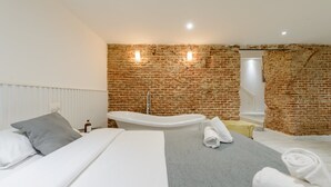 Une chambre moderne avec un mur en briques, un lit blanc, une baignoire et une petite salle de bain avec douche.