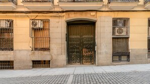 Une façade d’immeuble ornée d’une grande porte en bois sculpté, de fenêtres grillagées et d’un pavage en pierres.