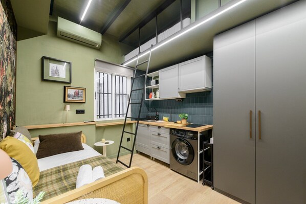 Cozy apartment with a bed, kitchenette, and air conditioning unit.