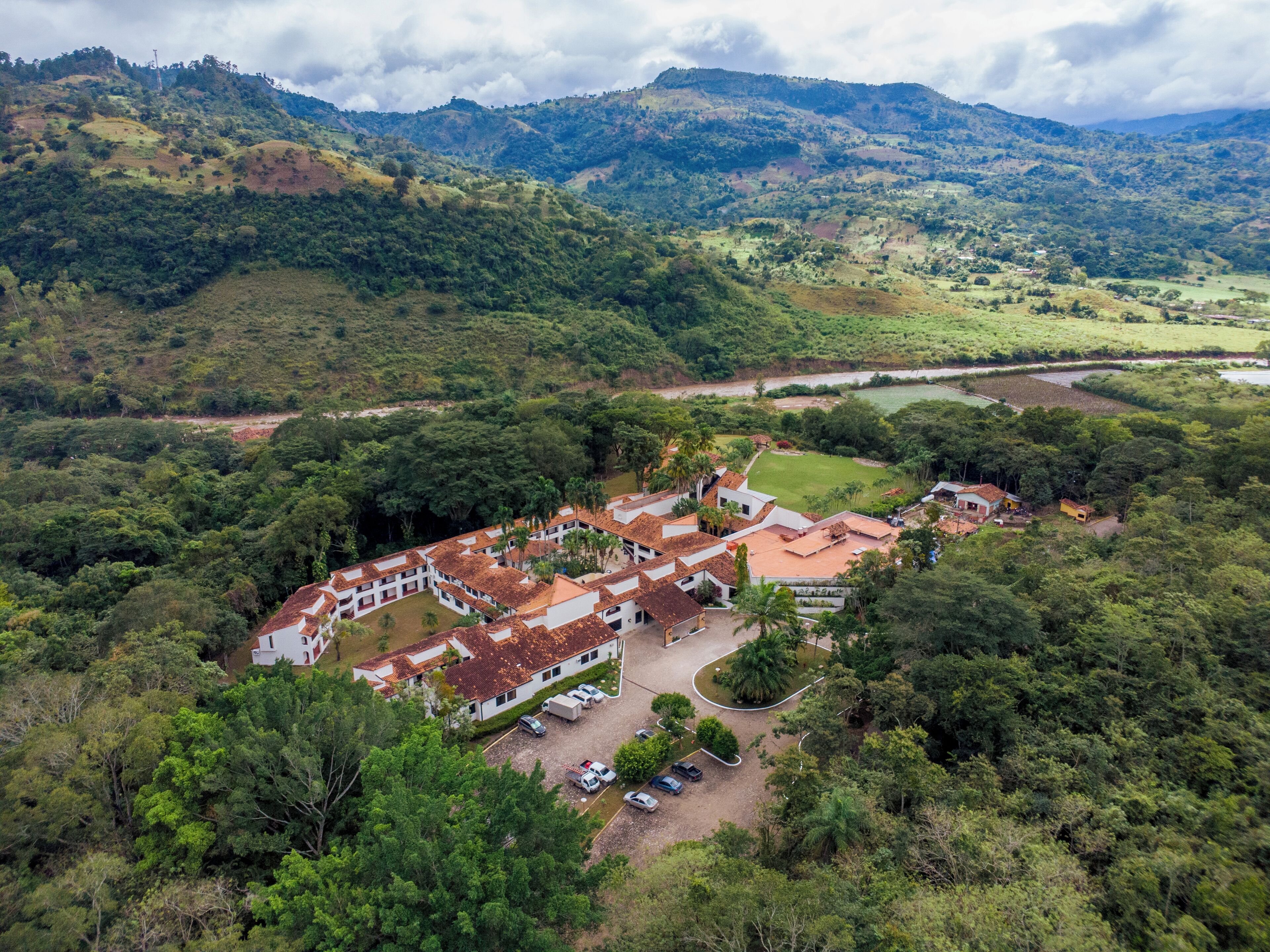 Vista aerea di un resort con diversi edifici, un’area parcheggio e una rigogliosa vegetazione circostante.