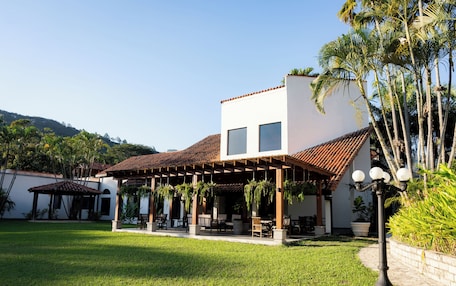 A two-story building with a tiled roof, a covered patio area with hanging plants, and a well-maintained lawn.