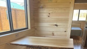 Una mesa de comedor de madera con dos taburetes, en una habitación con paredes de madera y una ventana.