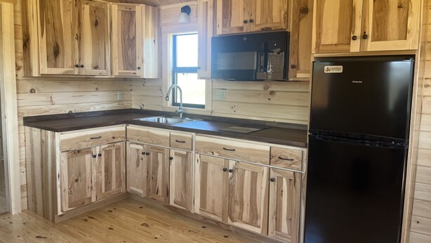 Una cocina con armarios de madera, un refrigerador negro y una ventana.