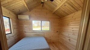 Una habitación de madera pequeña y acogedora con una cama individual, una ventana y un equipo de aire acondicionado.