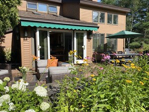 Una casa con porche cubierto, mobiliario exterior y una variedad de plantas y flores.