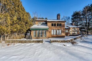 A two-story house with a stone foundation, wooden siding, and a green awning over the entrance. - Patio Condo Overlooking Highland Golf, Coach Road (Quechee)