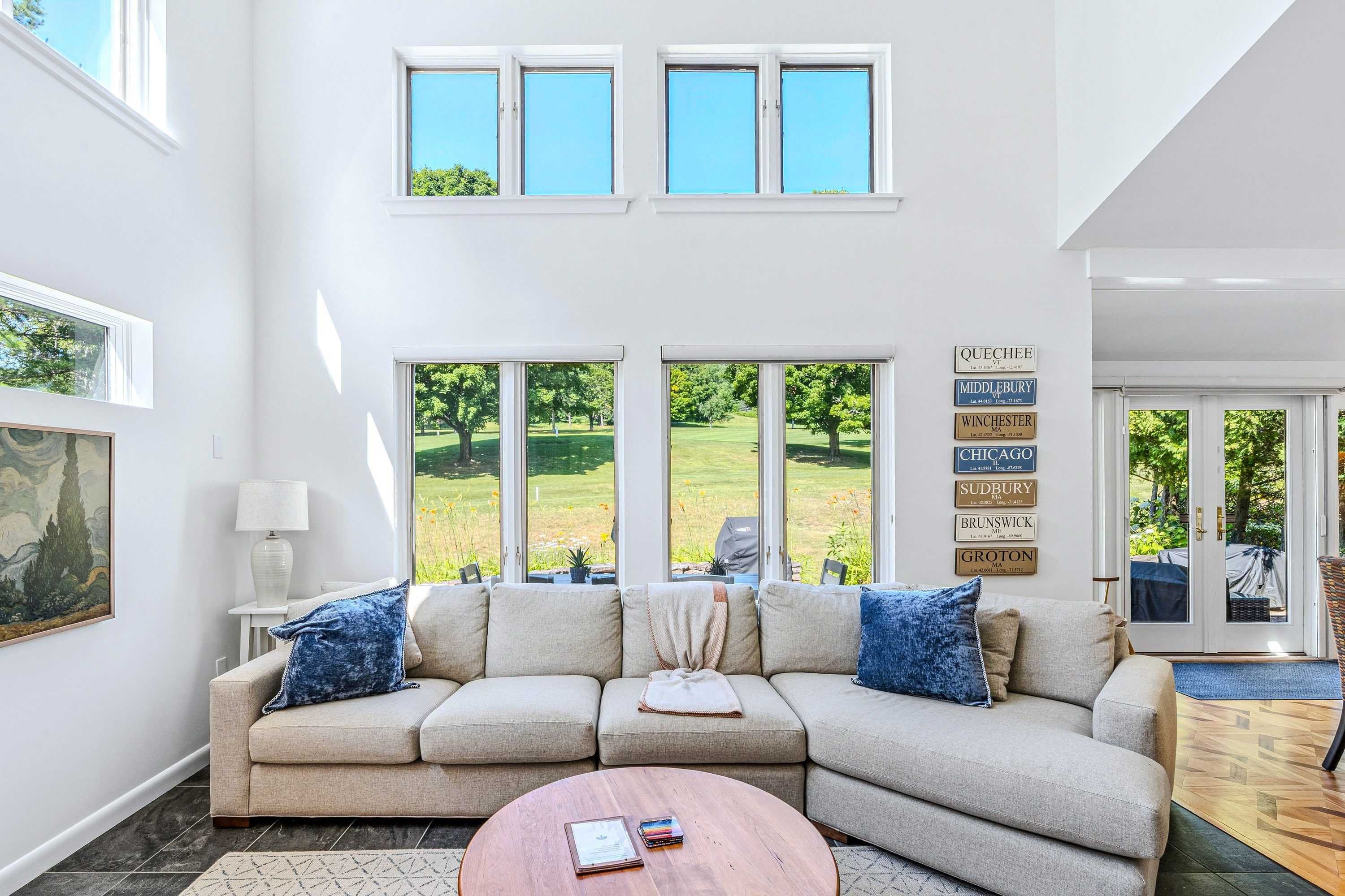 A living room with a sectional sofa, a coffee table, and a view of a green landscape through large windows.