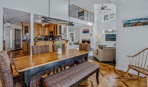 A spacious living area with a high ceiling, a dining table with benches, and a fireplace.