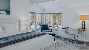 Habitación de hotel con cama, escritorio, silla y ventana con vista a árboles.
