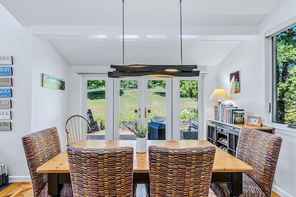 A dining area with a table and chairs, a pendant light, and a view of a garden through glass doors.