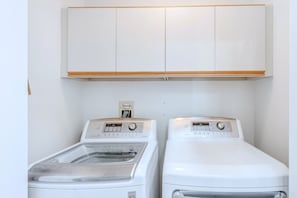A laundry room with two front-loading washing machines and a wooden cabinet above.