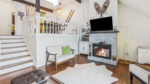 A living room with a fireplace, a staircase, a sofa, and a television. - Condo near Ski Hill with Club Access, Kingswood (Quechee)