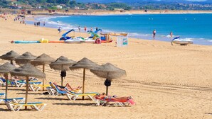 A beach with sun loungers and umbrellas, a lifeguard tower, and boats in the background. - Lagos Ocean View 2 With Pool by Homing (Lagos)