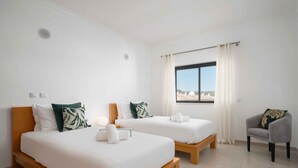 A hotel room with two beds, a chair, and a window with curtains. - Lagos Ocean View 2 With Pool by Homing (Lagos)
