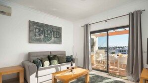 A living room with a sofa, a wooden coffee table, and a large window with curtains. - Lagos Ocean View 2 With Pool by Homing (Lagos)