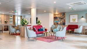 Een moderne lobby met een rode bank, grijze fauteuils, een bijzettafeltje en een boekenkast.