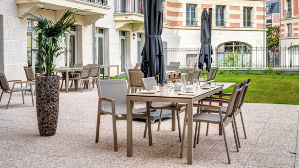 Een terras met tafels, stoelen, een plant in pot en parasols.