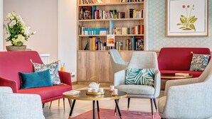 Een moderne woonkamer met rode banken, een grijze fauteuil en een boekenplank vol boeken.