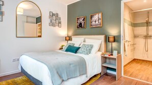 Een moderne slaapkamer met een bed, nachtkastjes, een spiegel, ingelijste foto's en een douchegedeelte.