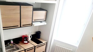 A compact living space with a kitchenette, a sofa with an orange pillow, and a small table. - Cosy mezzanine studio in Narbonne town center, close to beaches (Narbonne)