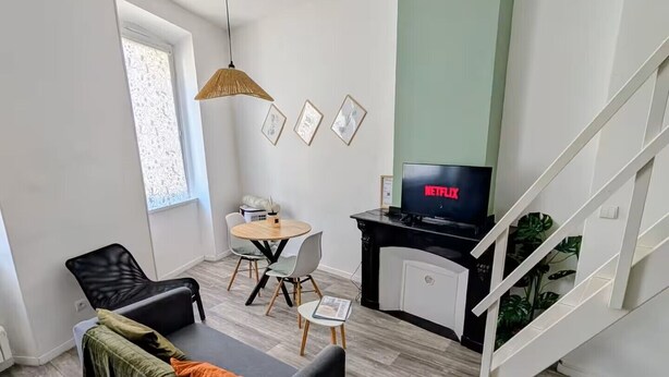 A modern living room with a sofa, a dining table, and a TV displaying 'NETFLIX'. - Cosy mezzanine studio in Narbonne town center, close to beaches (Narbonne)
