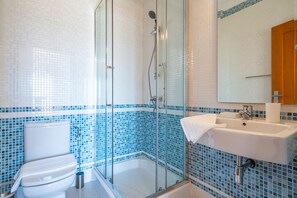 A bathroom with a glass-enclosed shower, a white toilet, and a sink with a mirror above it. - Lagos Ocean View 3 With Pool by Homing (Lagos)