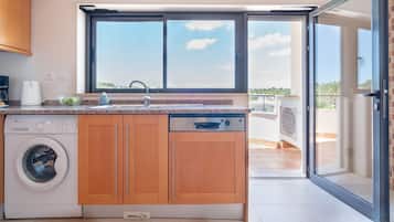 Cocina compacta con lavadora, pileta y ventana con vista a un balcón.